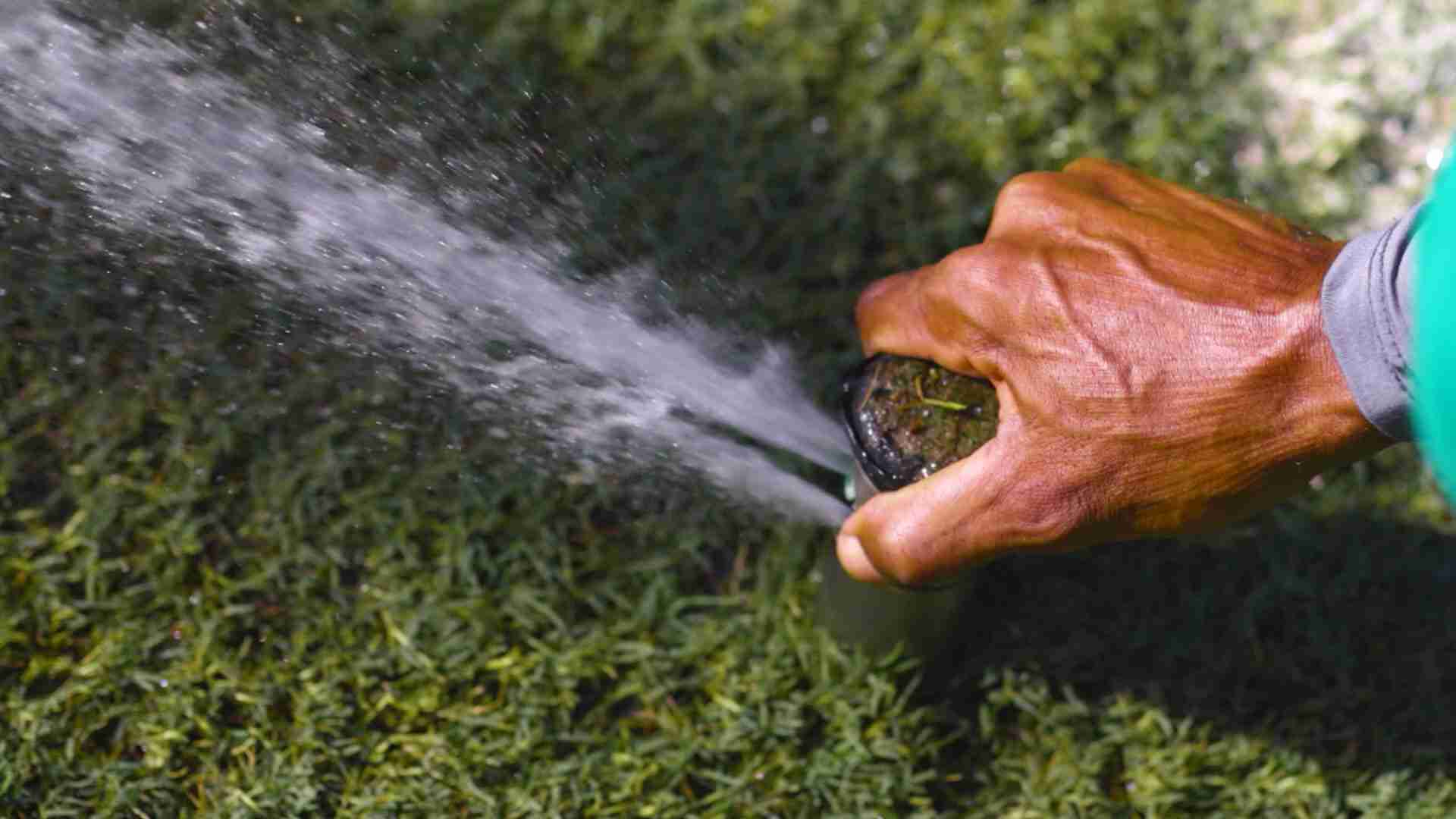 A hand adjusting an irrigation head squirting water