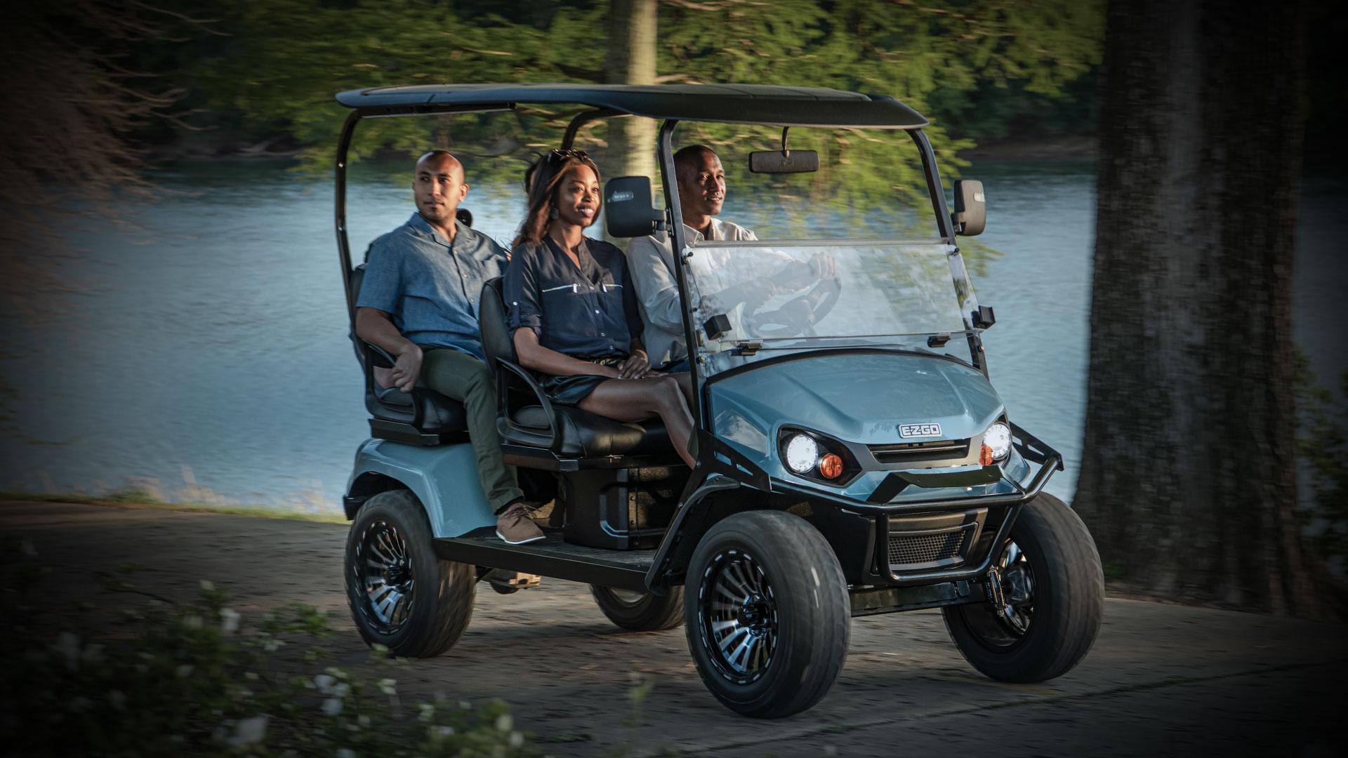 two men and a woman in a gold cart by the lake